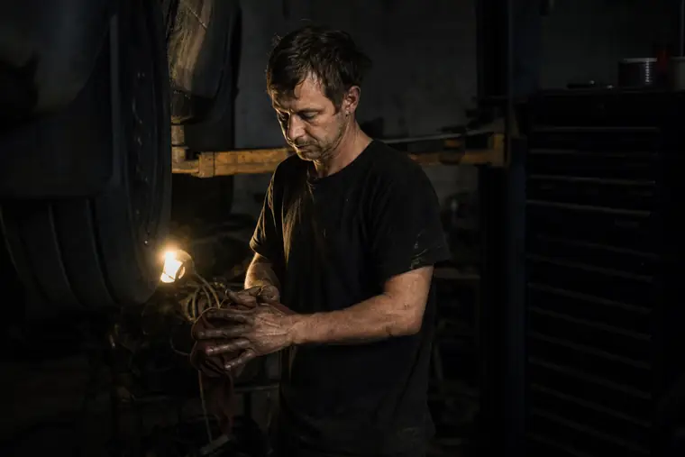 A mechanic beside a car on a lift in a two-bay repair shop