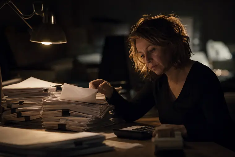 A stack of unpaid invoices under a desk lamp being flipped through